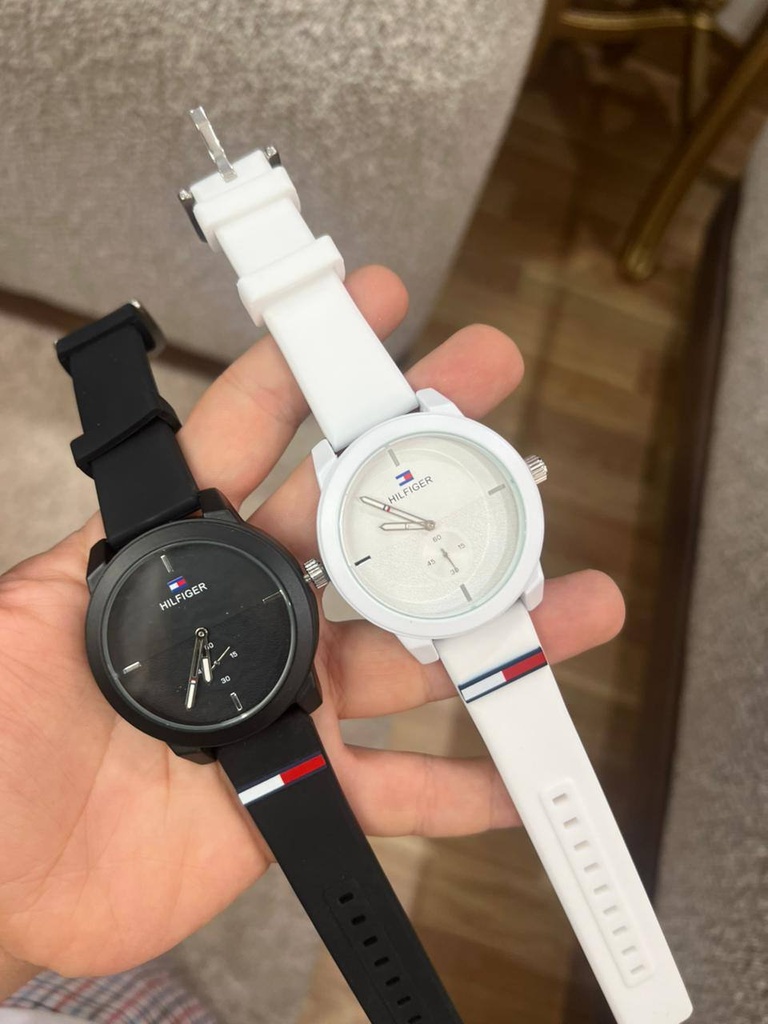 هذه الساعة هي ساعة تومي هيلفيغر (Tommy Hilfiger) الرجالية الرياضية باللون الأبيض الناصع، وتحديداً متتميز الساعة بتصميم كاجوال وعصري يناسب الإطلالات اليومية والرياضية، وتأتي بالمواصفات الأساسية التالية:الهيكل والسوار: مصنوعة من استيك سيليكون (مطاطي) مريح ومتين باللون الأبيض.المينا (القرص): باللون الأبيض مع شعار الماركة الشهير وعقارب واضحة، بالإضافة إلى نافذة دائرية صغيرة لعرض الثواني أو التوقيت الإضافي.اللمسة الجمالية: يزين السوار شريط صغير يحمل ألوان العلامة التجارية المميزة ( الأبيض، والاسود).